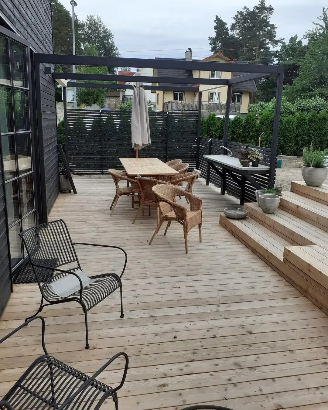 Trädäck med pergola i svart stål intill en svartmålad husfasad.