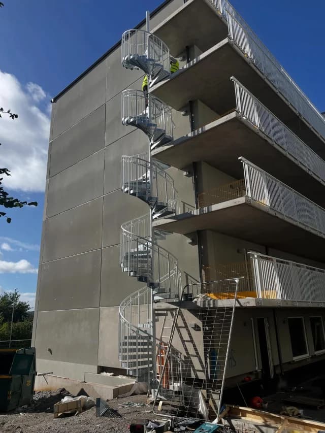 Spiraltrappa i galvaniserat stål monterad utanpå ett flerbostadshus med balkonger.